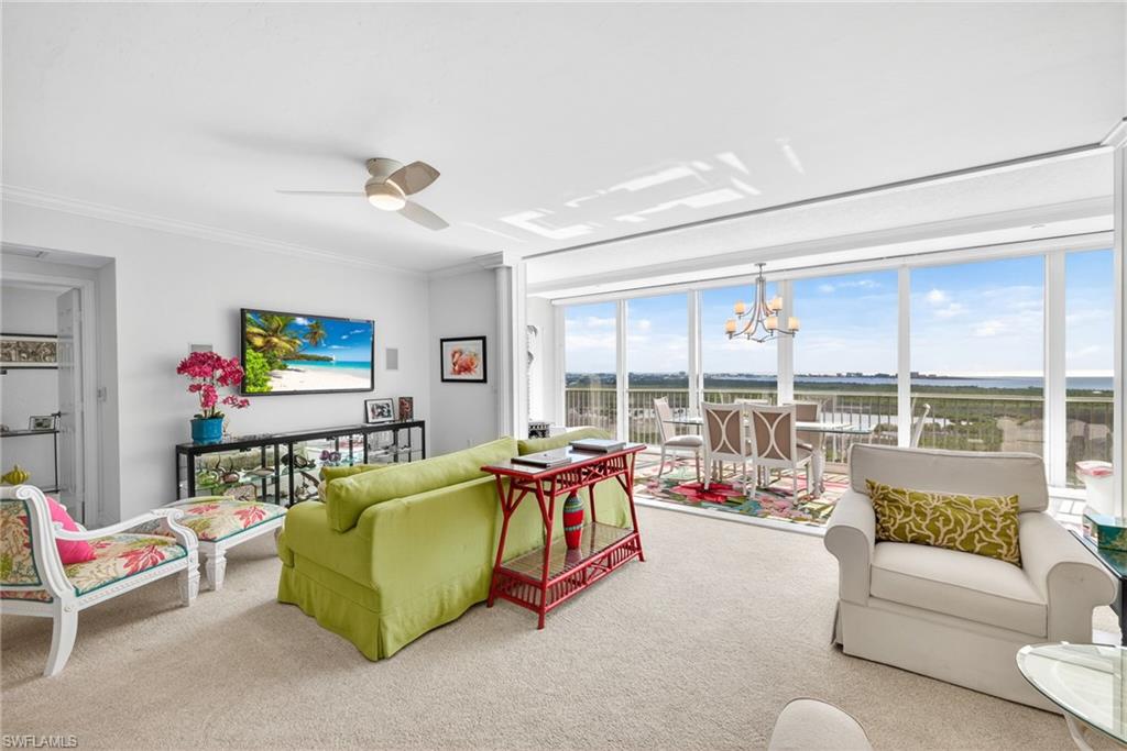 Carpeted living area with a chandelier, ceiling fan, and ornamental molding