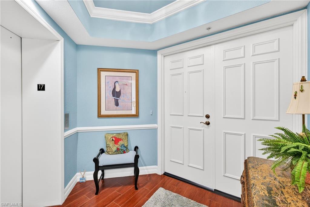 Exterior foyer featuring elevator, dark wood finished floors, a tray ceiling, and ornamental molding