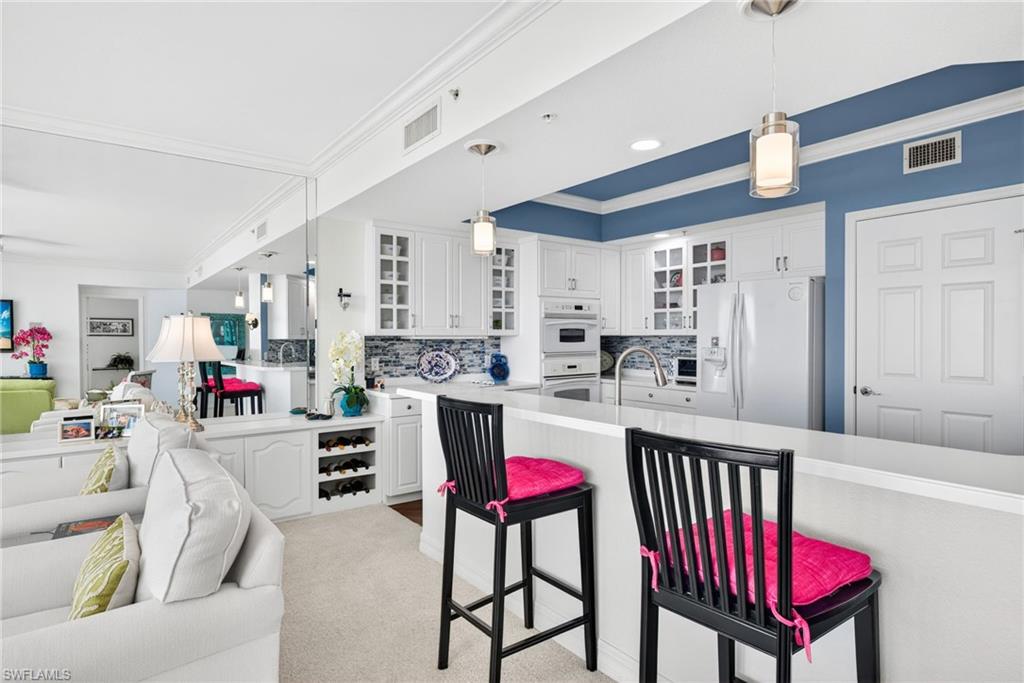 Kitchen with ornamental molding, glass insert cabinets, decorative light fixtures, open floor plan, and white appliances