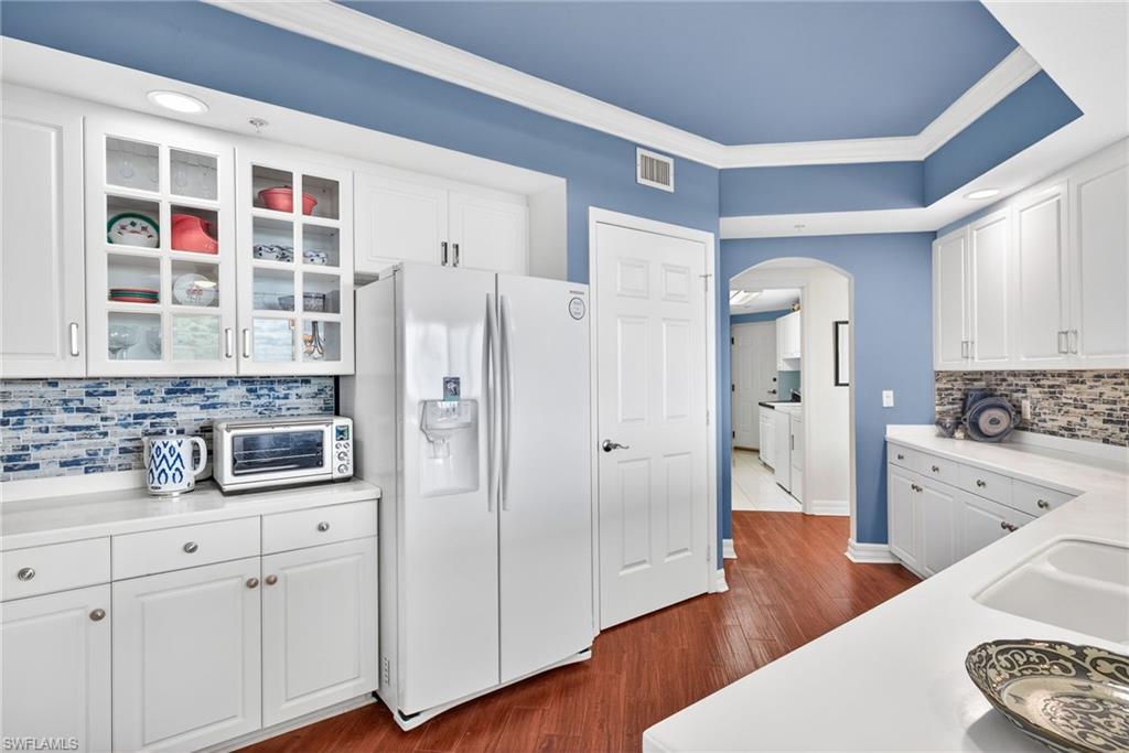Kitchen featuring decorative backsplash, white cabinetry, white refrigerator with ice dispenser, arched walkways, and crown molding
