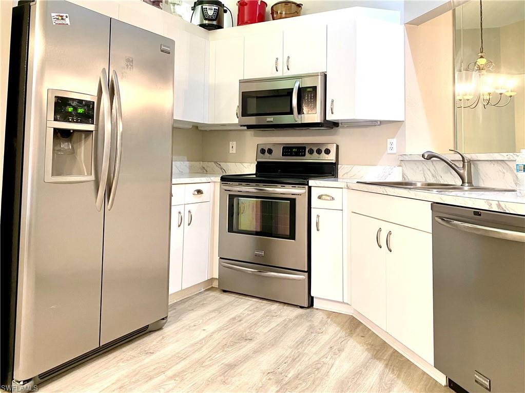 Kitchen with light hardwood / wood-style flooring, hanging light fixtures, sink, white cabinetry, and appliances with stainless steel finishes
