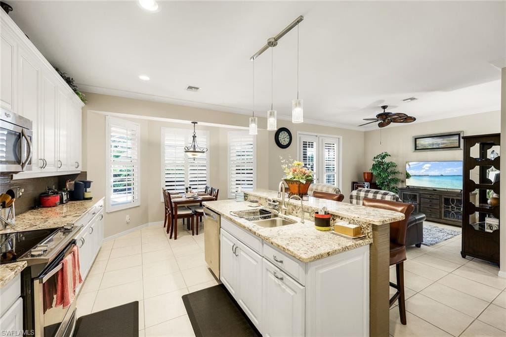 Kitchen with white cabinetry, a kitchen bar, light stone countertops, light tile patterned floors, and crown molding