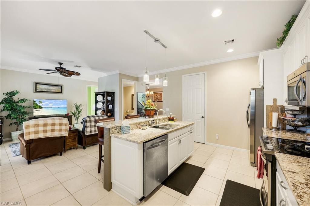 Kitchen featuring white cabinets, light stone counters, decorative light fixtures, a kitchen island with sink, and crown molding