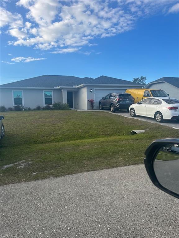 Single story home featuring a garage, stucco siding, a front yard, and driveway