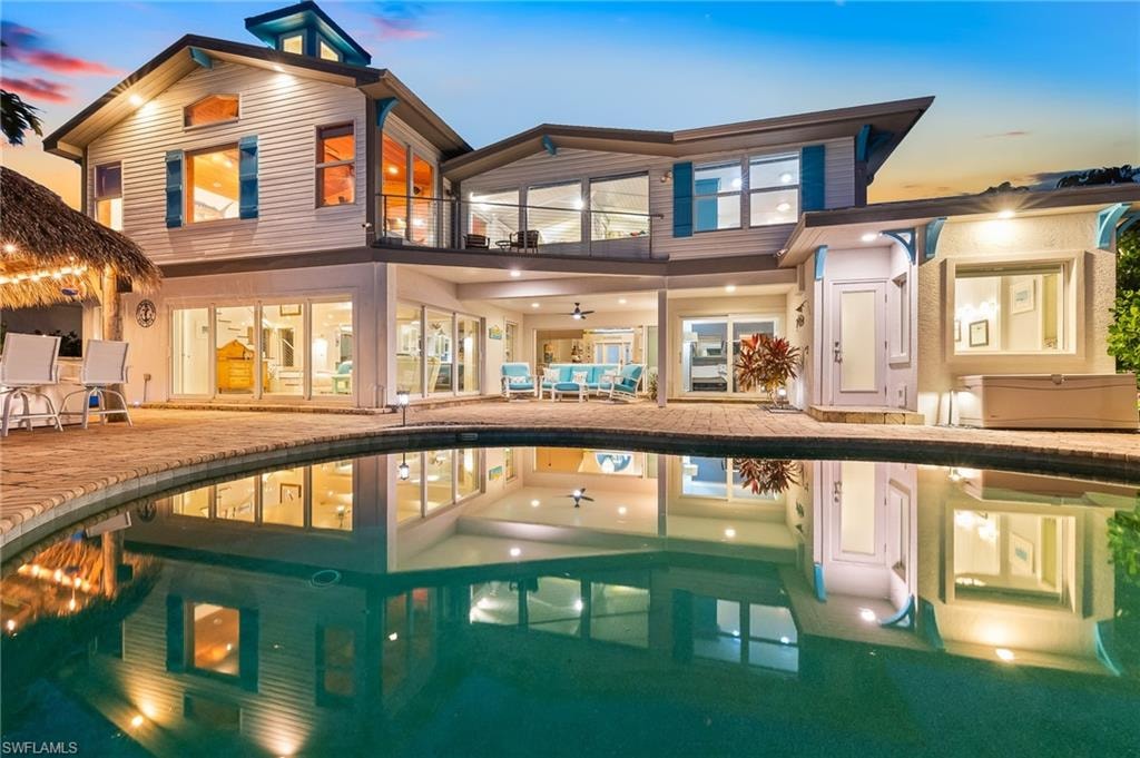 Back of property at dusk with a patio, an outdoor pool, a balcony, and outdoor lounge area