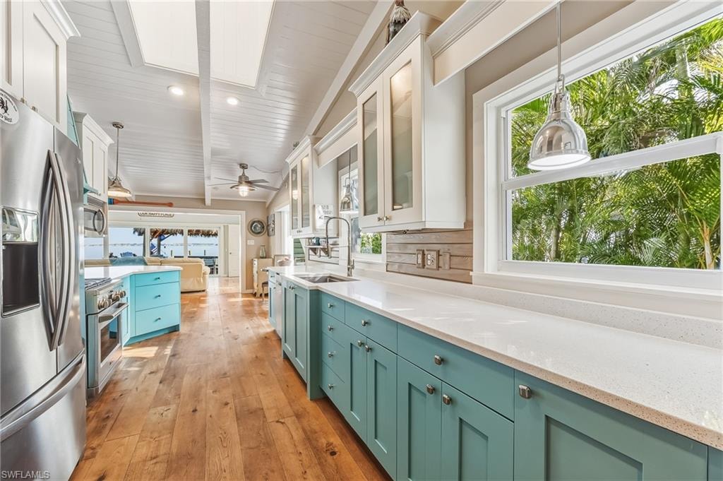Kitchen with decorative light fixtures, glass insert cabinets, white cabinetry, stainless steel appliances, and light stone counters