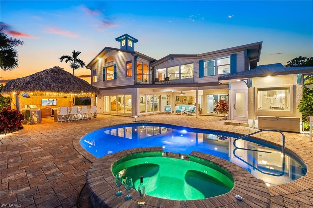 Back of property at dusk with a patio area, a balcony, a pool with connected hot tub, ceiling fan, and an outdoor living space