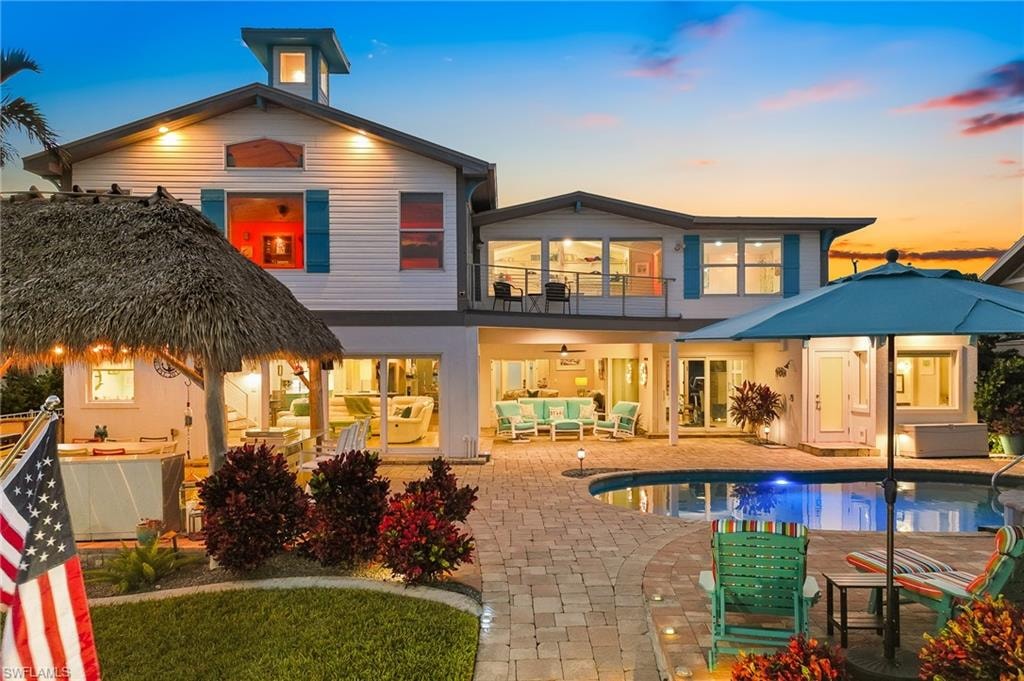 Back of house at dusk featuring outdoor lounge area, a balcony, a patio area, an outdoor pool, and ceiling fan