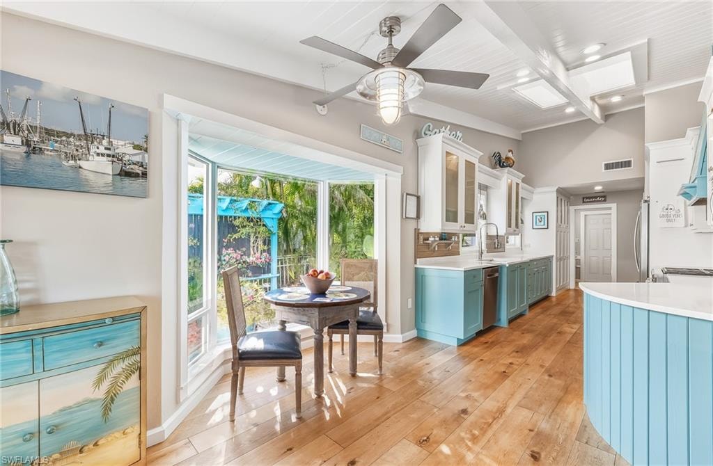 Kitchen with beamed ceiling, white cabinets, light wood-style floors, ceiling fan, and light stone counters