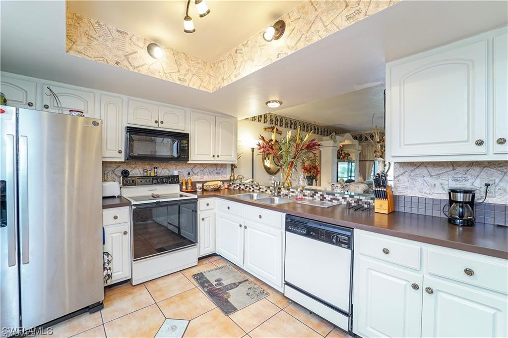 Kitchen with white appliances, dark countertops, white cabinetry, light tile patterned floors, and tasteful backsplash