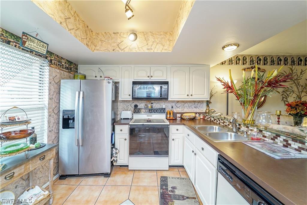 Kitchen featuring a raised ceiling, white appliances, white cabinets, light tile patterned flooring, and dark countertops