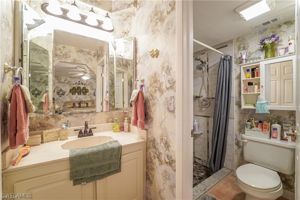 Full bath featuring vanity, a stall shower, wallpapered walls, and a ceiling fan