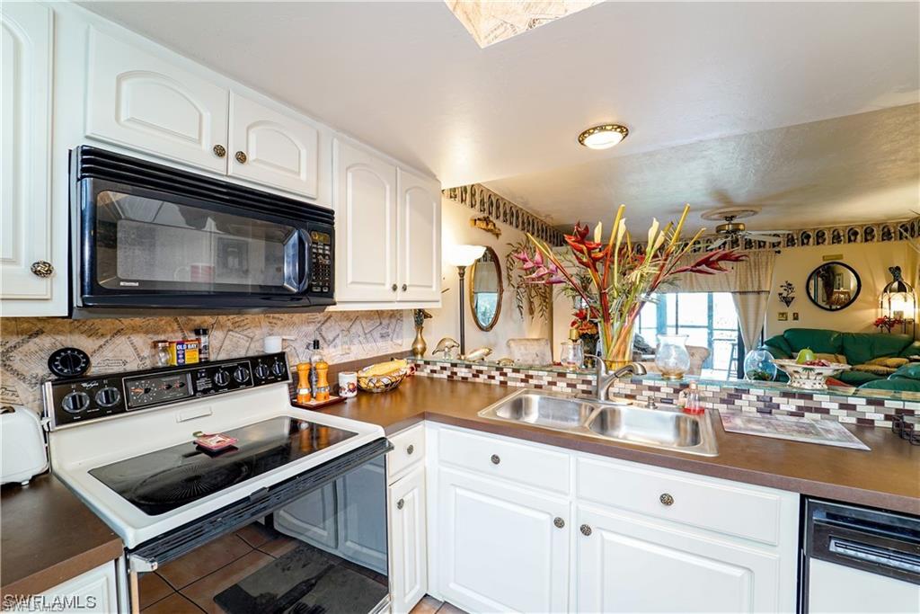 Kitchen with electric range oven, dark countertops, and white cabinetry