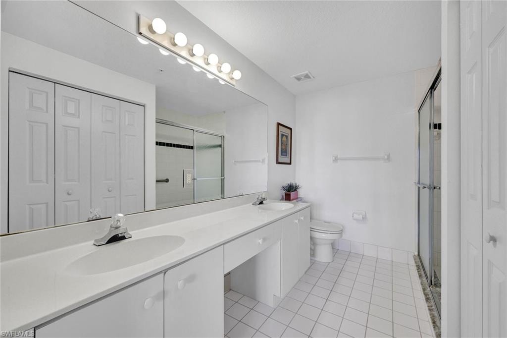 Bathroom featuring a closet, double vanity, light tile patterned floors, and a stall shower