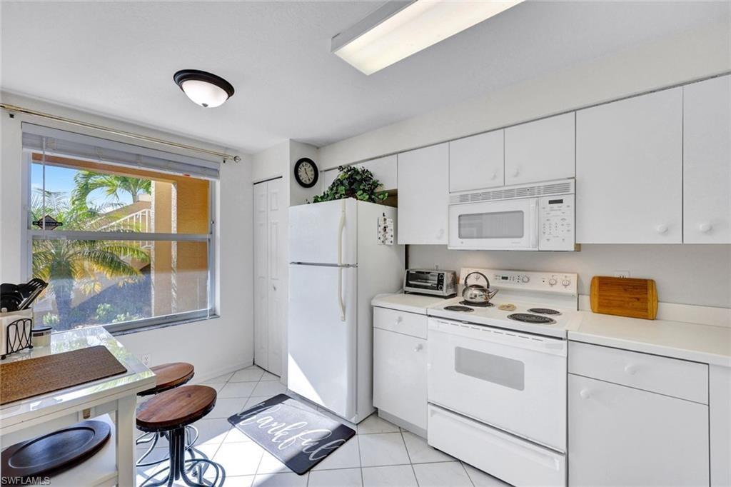 Kitchen featuring white appliances, light countertops, white cabinets, and light tile patterned floors