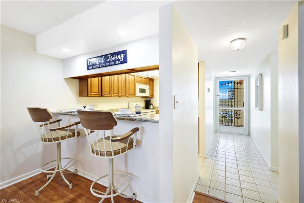 Kitchen with a kitchen bar, brown cabinetry, white appliances, a peninsula, and light stone counters