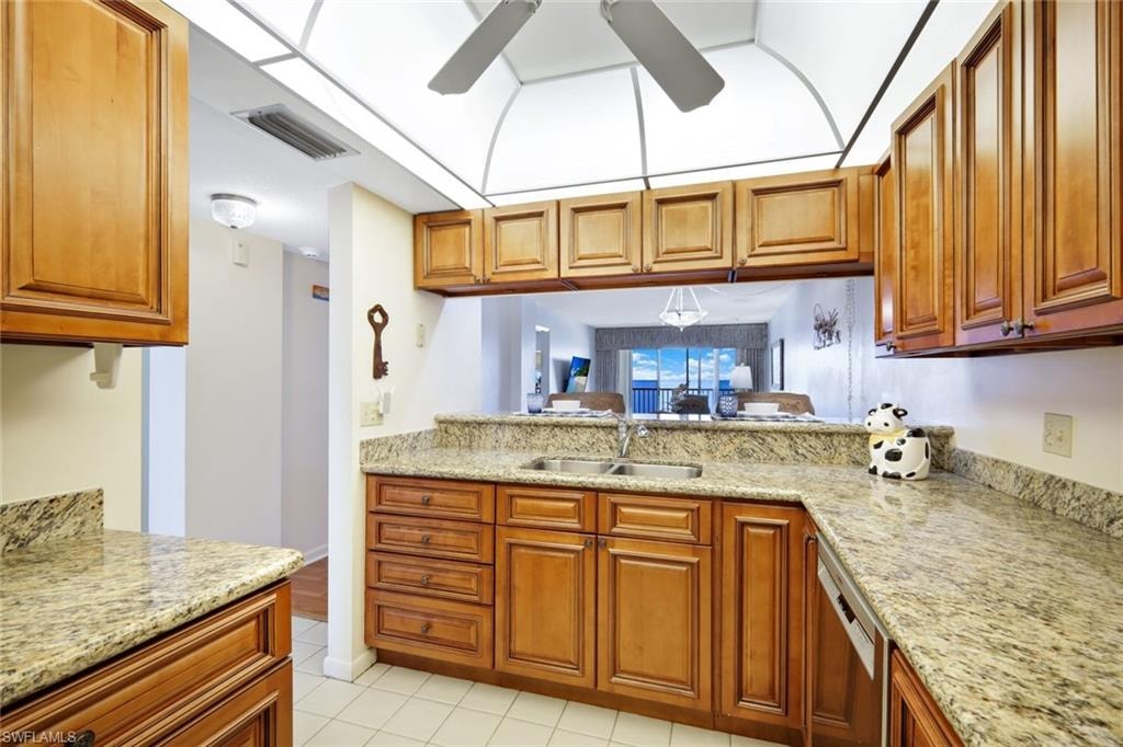 Kitchen with light stone countertops, stainless steel dishwasher, brown cabinetry, and light tile patterned flooring