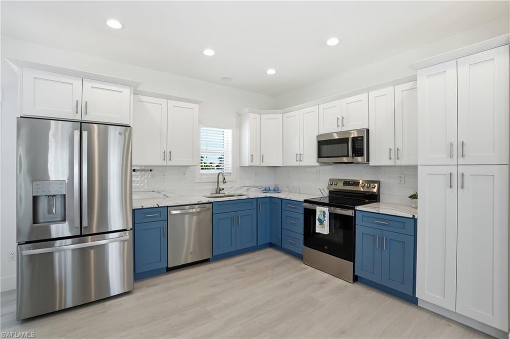 Contemporary kitchen featuring two-tone cabinetry, stainless steel appliances, marble-look countertops, a geometric tile backsplash, and light wood-finish flooring - Virtually Edited Image