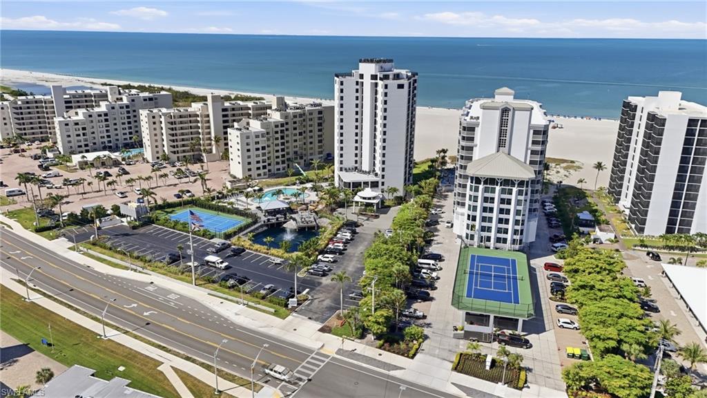 Coastal property featuring multiple high-rise buildings, an outdoor swimming pool, tennis court, and direct beach access - Virtually Edited Image