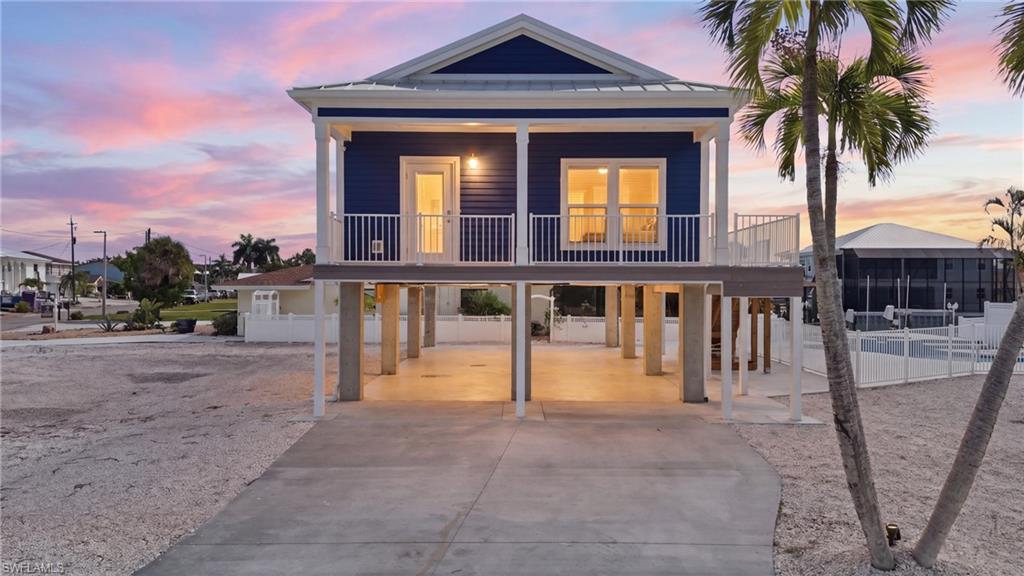 Elevated coastal residence featuring a deep blue exterior, white trim, and a covered ground-level parking area - Virtually Edited Image