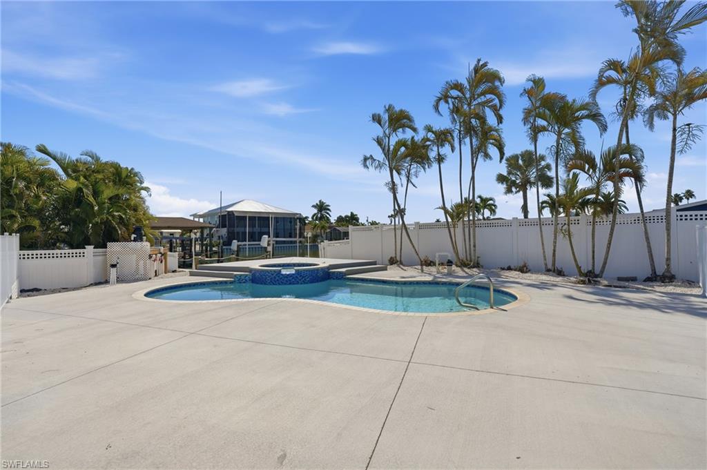 Curved swimming pool with an integrated spa, surrounded by expansive concrete decking - Virtually Edited Image