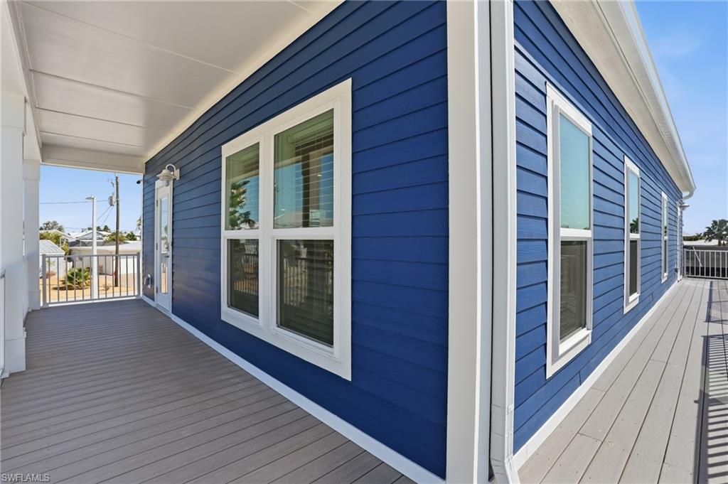 Exterior featuring blue horizontal siding, multiple windows with white trim, a covered porch with white columns, and gray decking - Virtually Edited Image
