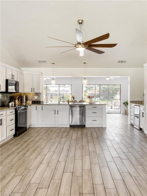 Kitchen featuring white cabinetry, black appliances, decorative backsplash, plenty of natural light, and vaulted ceiling