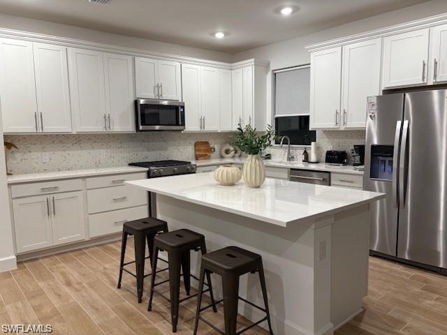 Kitchen featuring appliances with stainless steel finishes, a breakfast bar, wood finish floors, a kitchen island, and white cabinetry