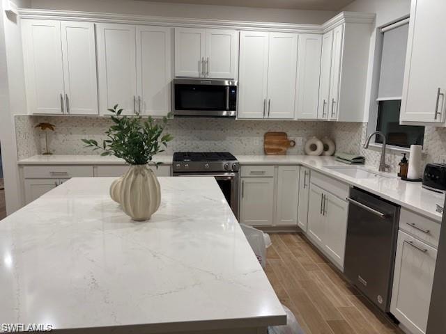 Kitchen with stainless steel appliances, white cabinetry, wood finish floors, light stone countertops, and backsplash