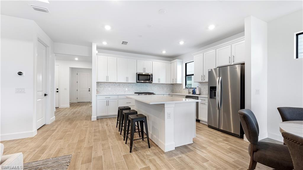 Kitchen featuring stainless steel appliances, a breakfast bar, light wood-style flooring, a kitchen island, and white cabinets