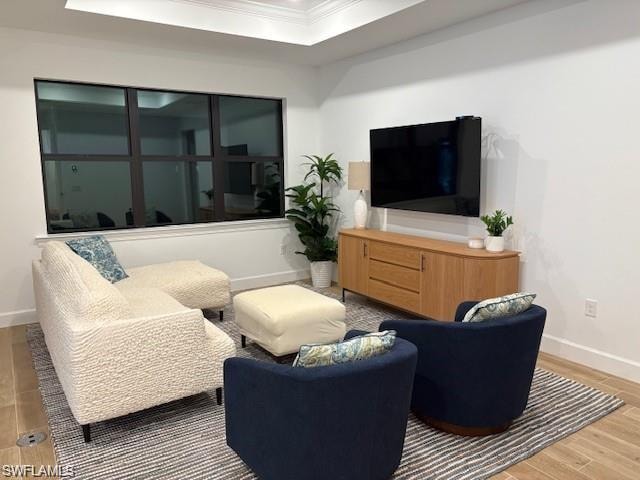 Living room with a tray ceiling, wood finished floors, and ornamental molding