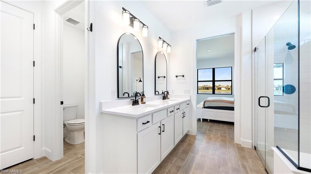 Ensuite bathroom featuring double vanity, wood tiled floors, and a stall shower