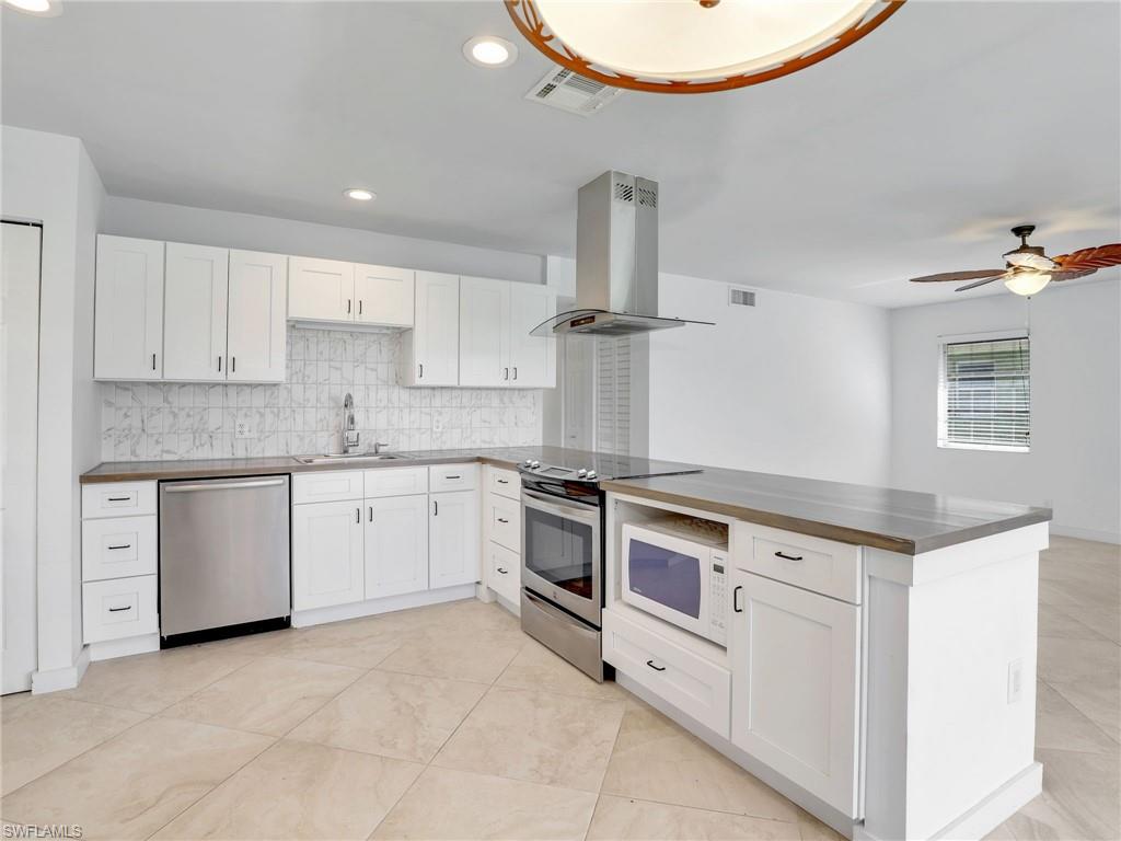 Kitchen featuring island exhaust hood, appliances with stainless steel finishes, white cabinets, backsplash, and recessed lighting