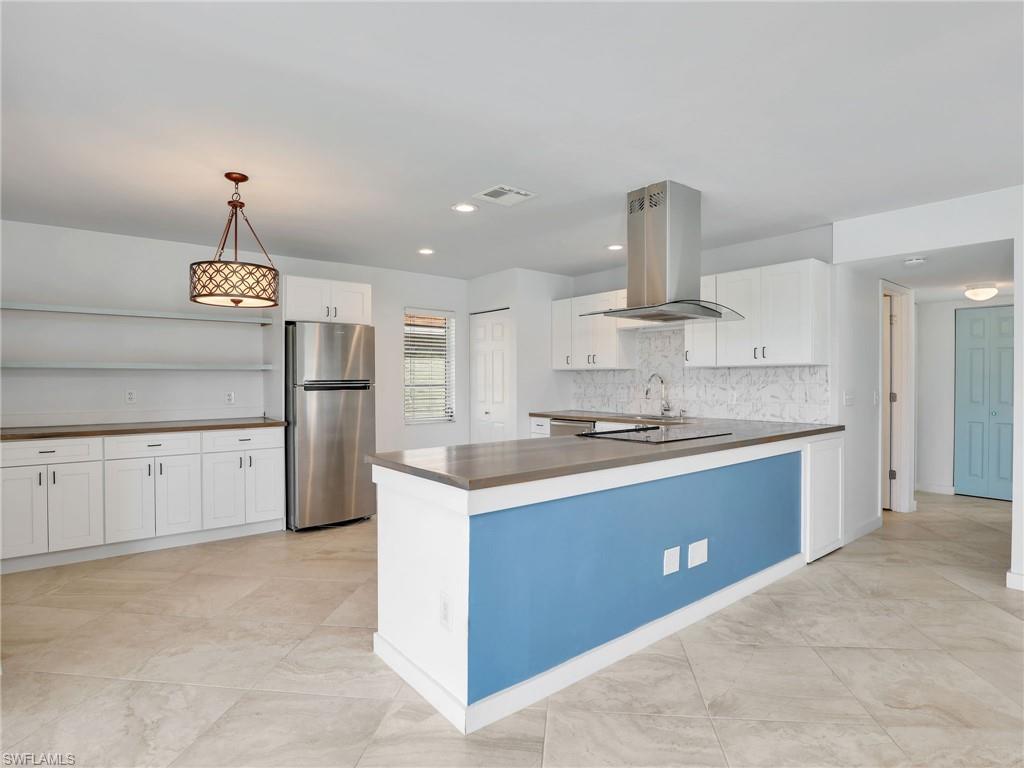 Kitchen featuring island exhaust hood, freestanding refrigerator, white cabinets, dark countertops, and decorative light fixtures