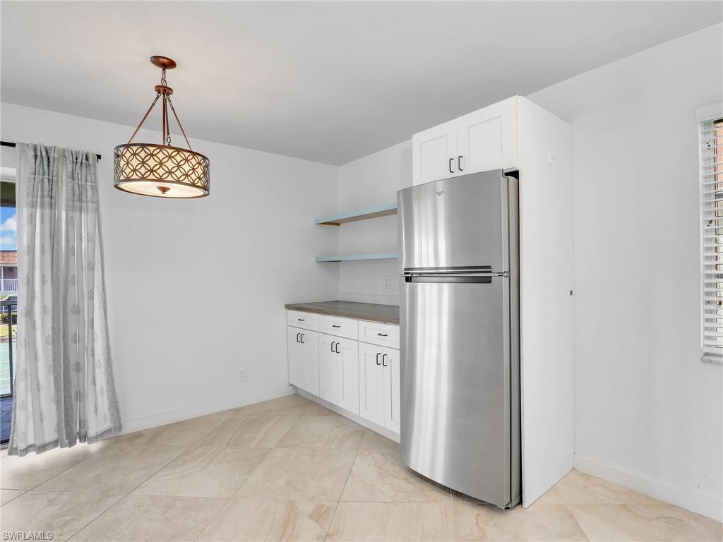 Kitchen featuring freestanding refrigerator, open shelves, white cabinets, and pendant lighting