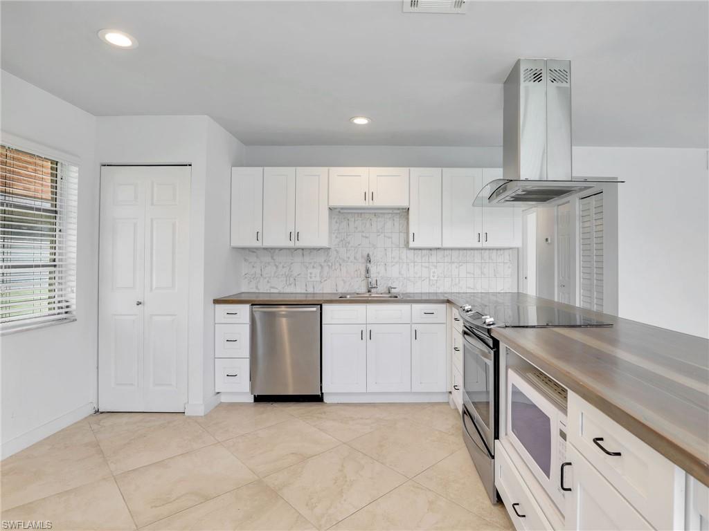 Kitchen featuring stainless steel appliances, island exhaust hood, decorative backsplash, white cabinets, and wood counters