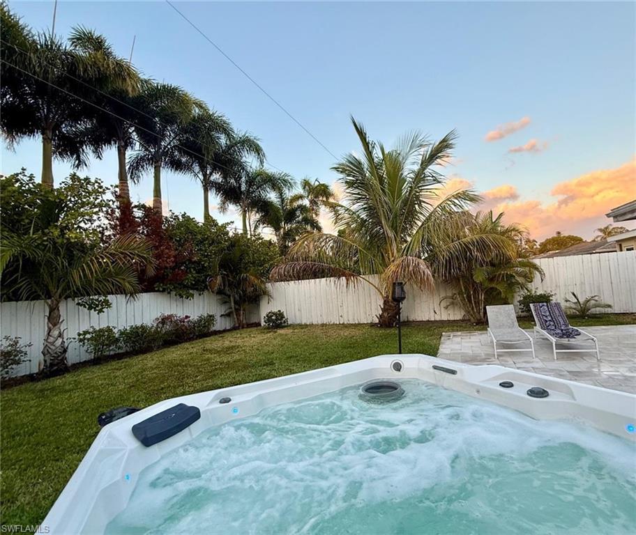 Pool at dusk with a fenced backyard and a hot tub