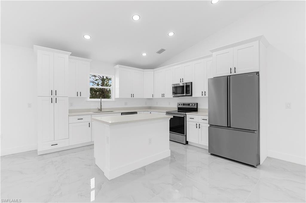 Kitchen with appliances with stainless steel finishes, white cabinetry, recessed lighting, a kitchen island, and light marble finish floors