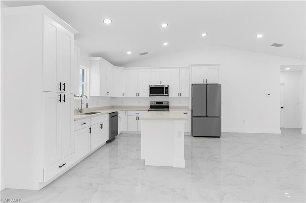 Kitchen featuring appliances with stainless steel finishes, a center island, white cabinets, light marble finish flooring, and vaulted ceiling