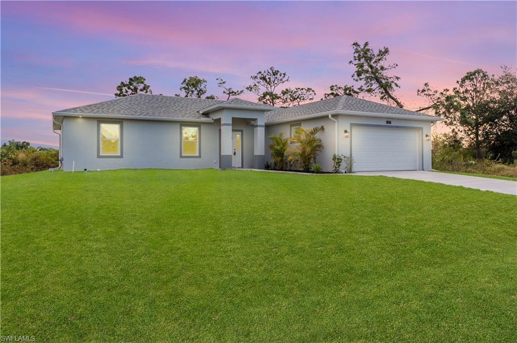 View of front of house featuring a yard, driveway, an attached garage, and stucco siding