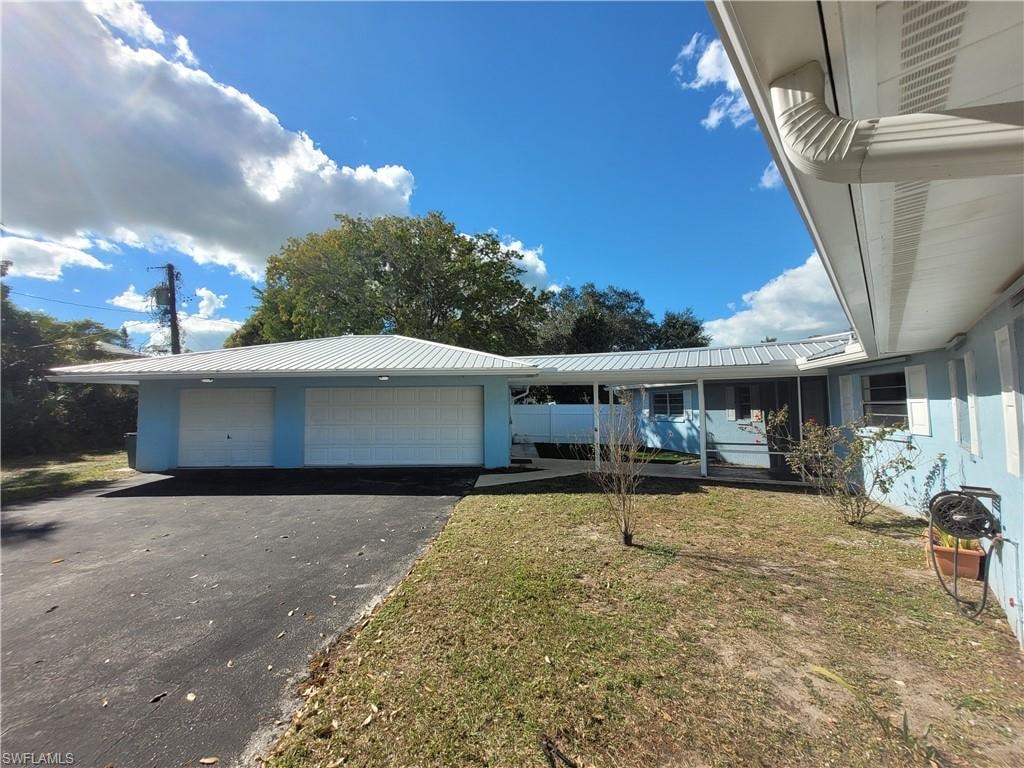View of front facade with an attached garage, a metal roof, a front yard, and driveway