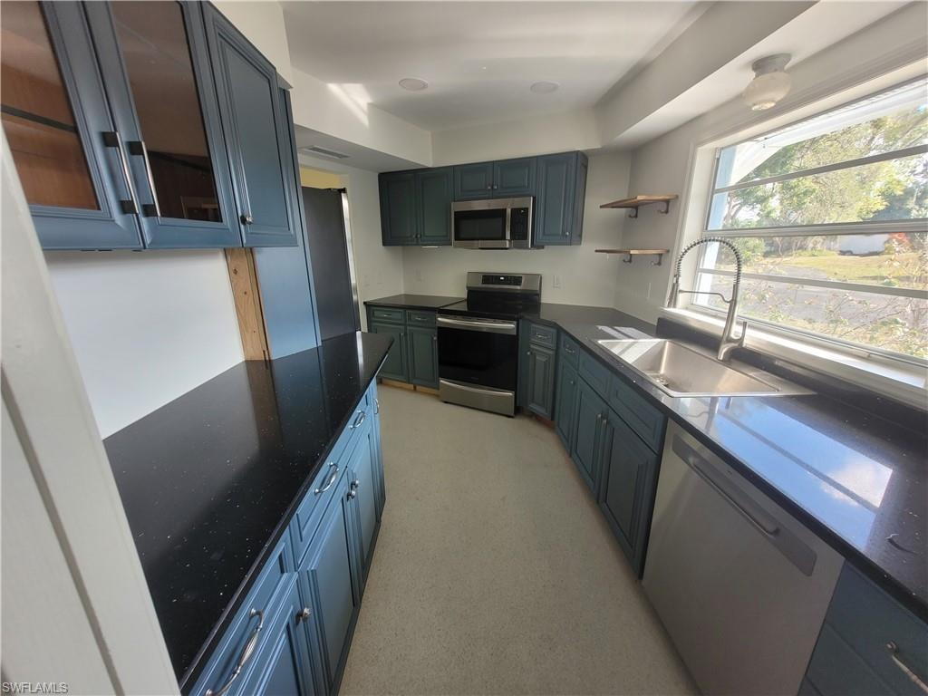 Kitchen with appliances with stainless steel finishes, glass insert cabinets, open shelves, dark stone countertops, and blue cabinetry