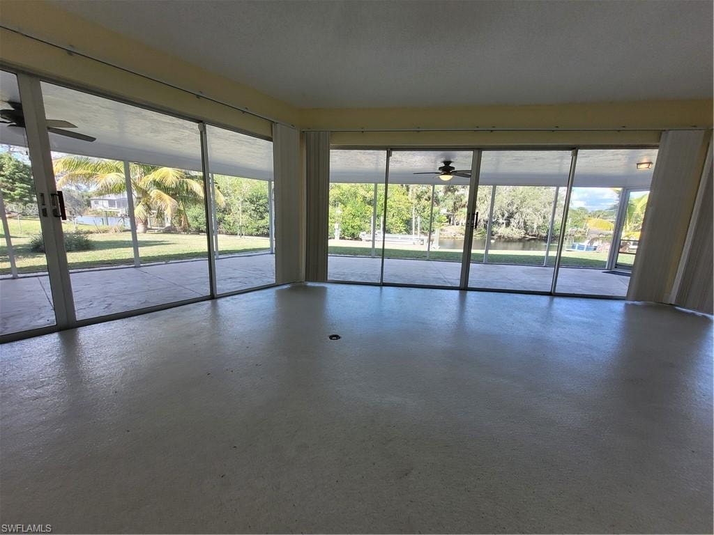 Spare room with a ceiling fan, concrete flooring, a sunroom, and healthy amount of natural light
