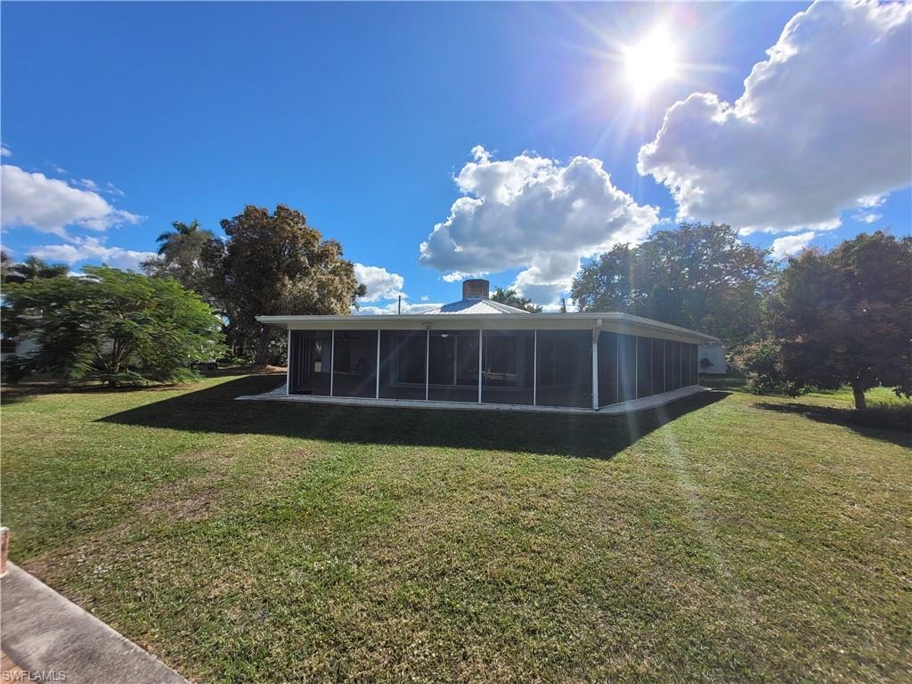 Rear view of property with a lawn, a chimney, and a sunroom