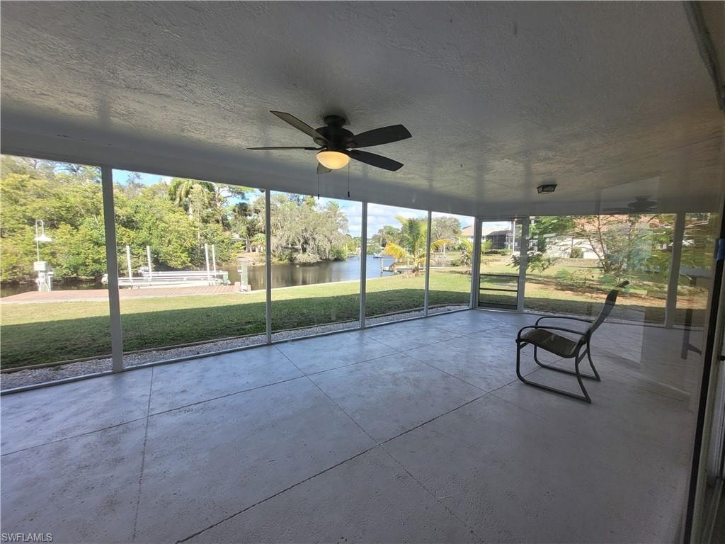 Unfurnished sunroom featuring a ceiling fan and a water view