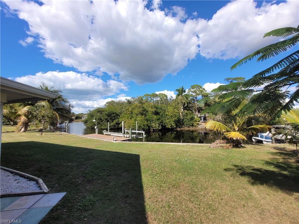 View of green lawn with boat lift, a boat dock, and a water view