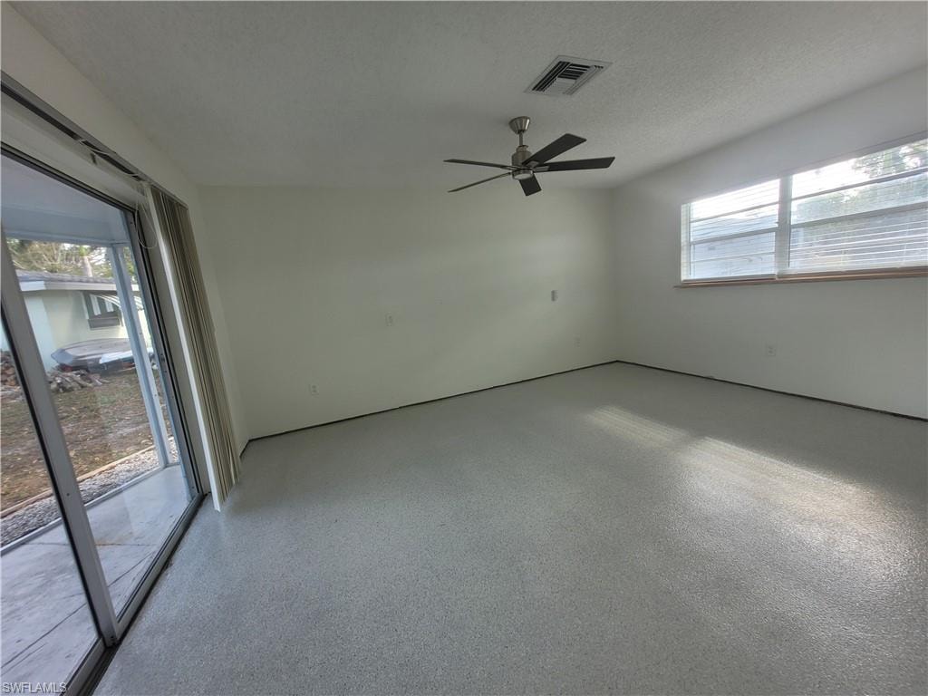 Unfurnished room with plenty of natural light, speckle patterned floor, a textured ceiling, and a ceiling fan