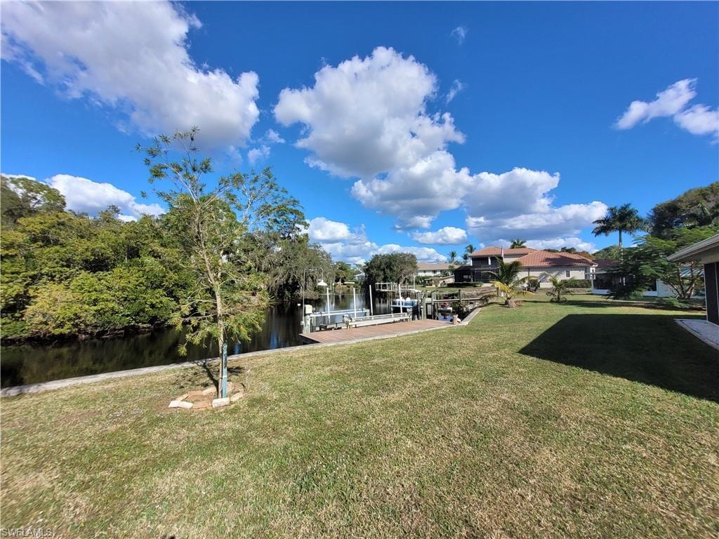 View of green lawn featuring a water view, a boat dock, and boat lift