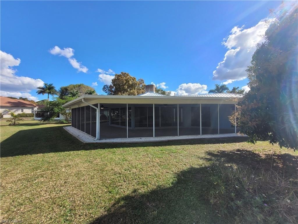Rear view of house featuring a lawn, a metal roof, and a sunroom