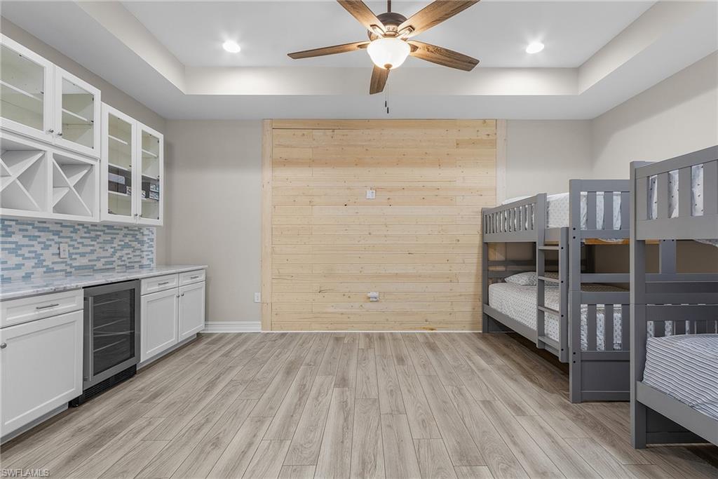 Upstairs Bar area featuring glass insert cabinets, white cabinetry, beverage cooler, light wood-type flooring, and a raised ceiling